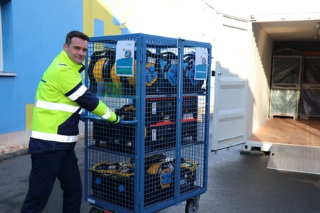 Arbeiter in gelber Warnjacke schiebt Gitterbox